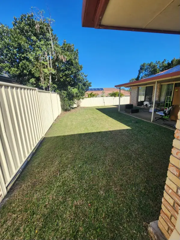 Neatly mown backyard lawn beside a covered patio and cream Colorbond fence