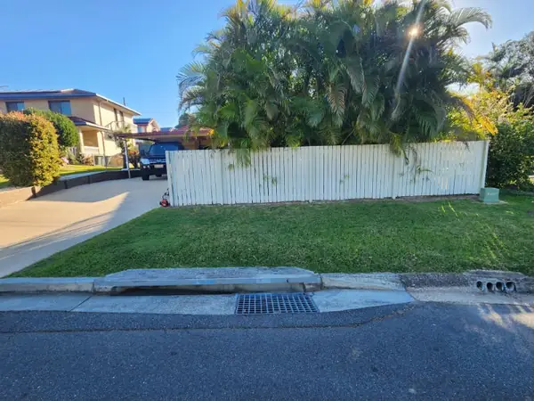 Front lawn mown in even stripes along a white boundary fence