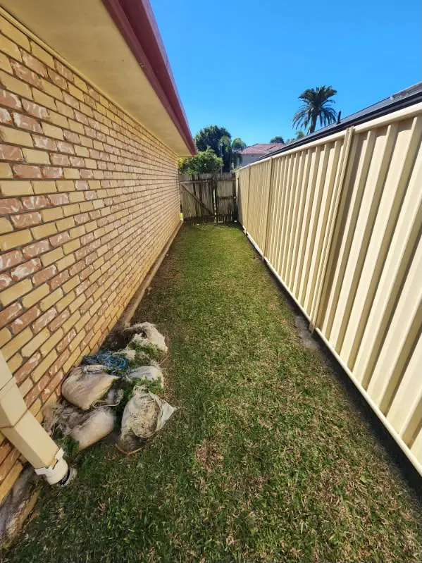 Narrow side access strip mown between a brick wall and Colorbond fence