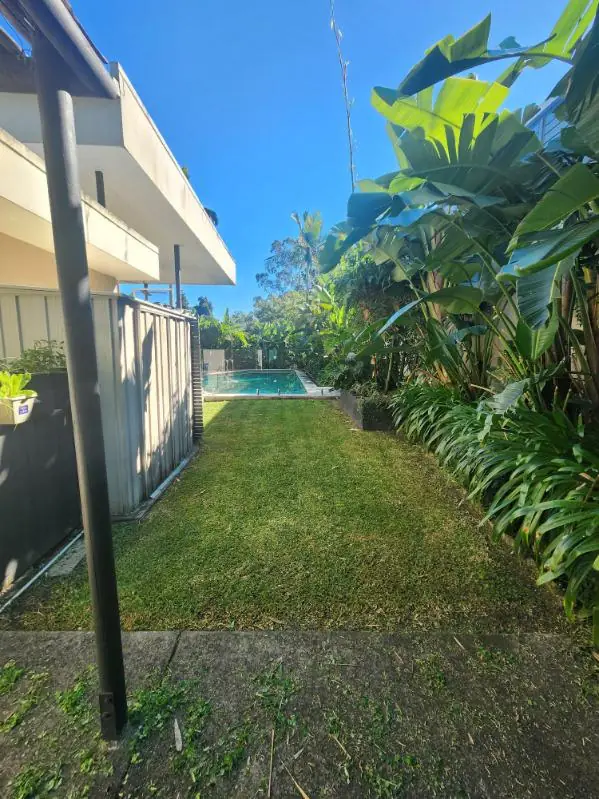 Narrow side lawn mown neatly along a garden bed leading to a swimming pool
