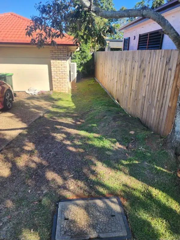 Shaded side lawn mown clean along a timber boundary fence